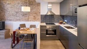 A modern kitchen with a brick wall, stainless steel appliances, and a dining area with a table and chairs. - Pau Claris | Design 1BR home near Paseo de Gracia (Barcelona)