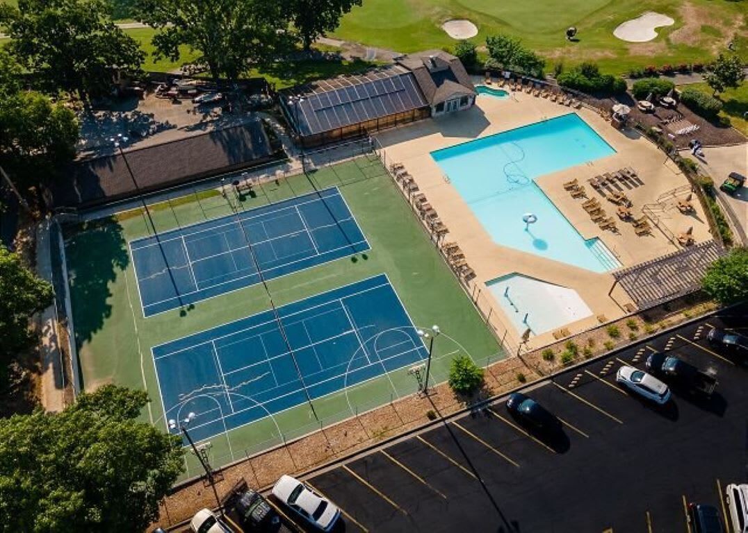Vue aérienne d’un complexe sportif comprenant des courts de tennis, une piscine et un parking.