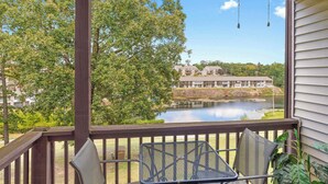 A wooden deck with two metal chairs and a table, overlooking a lake with buildings in the background.