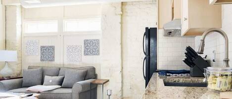 Una cocina con encimera de granito, un refrigerador y un comedor con sofá y una mesa pequeña.