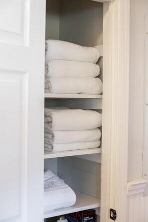 A white closet with shelves holding neatly folded white towels.