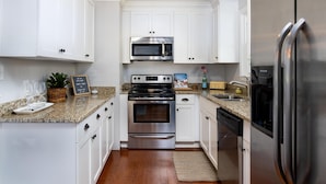 A modern kitchen with white cabinets, stainless steel appliances, granite countertops, and a built-in oven. - Palm Key - Cozy Coastal Charm (Charleston)