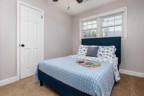 Une chambre à coucher avec un lit, une fenêtre avec des stores, une porte et un ventilateur de plafond.