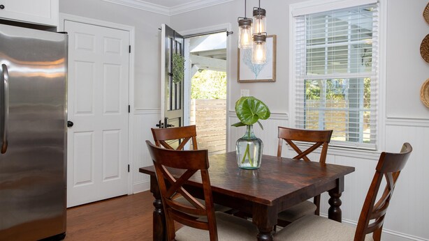 A dining area with a wooden table, four chairs, a vase with a plant, and a stainless steel refrigerator. - Palm Key - Cozy Coastal Charm (Charleston)
