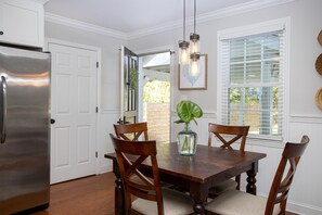 A dining area with a wooden table, four chairs, a vase with a plant, and a stainless steel refrigerator.