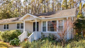 A two-story house with a front porch, a covered entryway, and a small garden area with various plants. - Palm Key - Cozy Coastal Charm (Charleston)