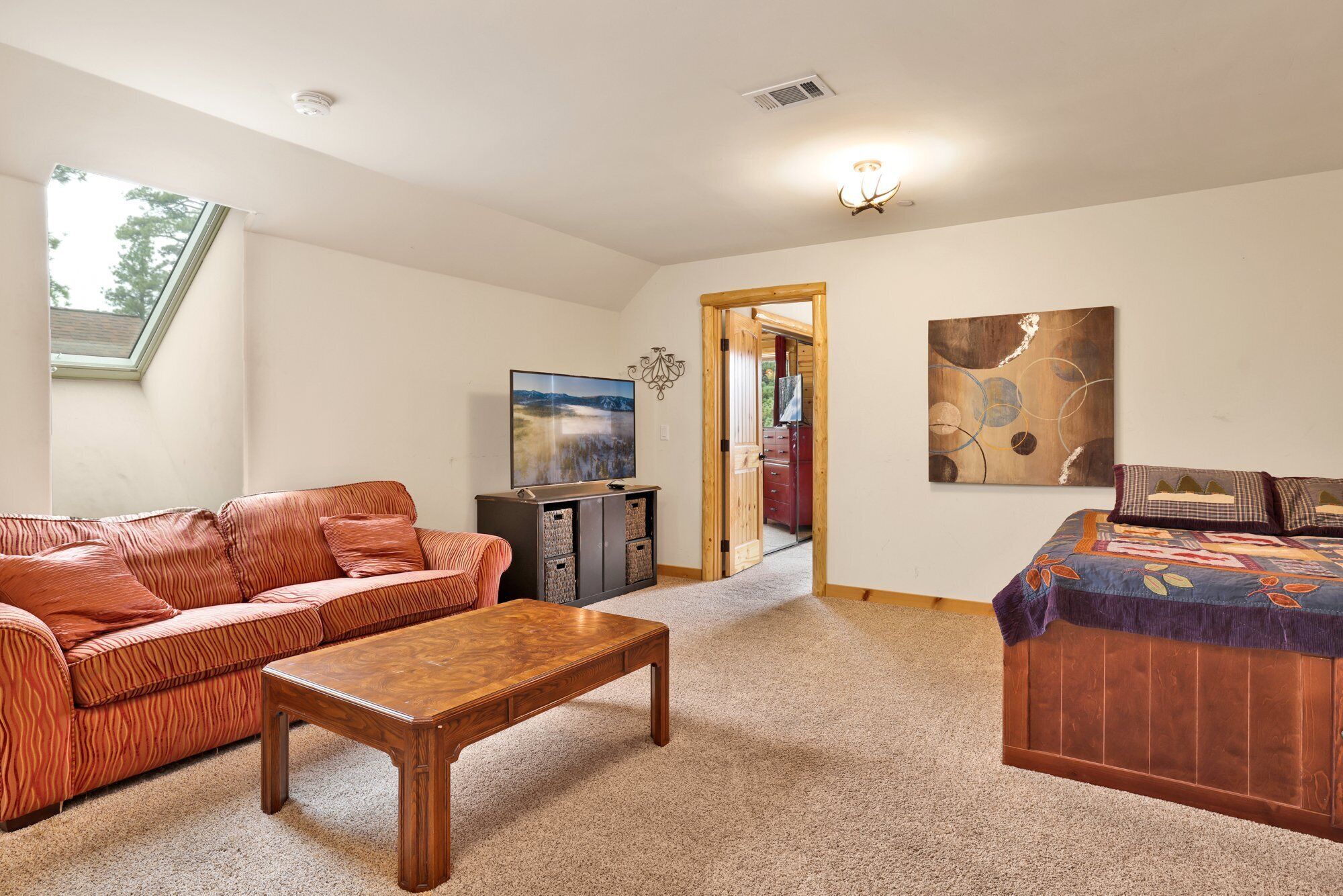 A living room with a sofa, a coffee table, a bed, and a painting on the wall.
