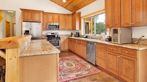 A kitchen with wooden cabinets, granite countertops, stainless steel appliances, and a red patterned rug. - Eagle Ridge Views #1648 (Big Bear Lake)