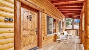 A log cabin with a wooden door, a porch with two rocking chairs, and a view of the surrounding landscape. - Eagle Ridge Views #1648 (Big Bear Lake)