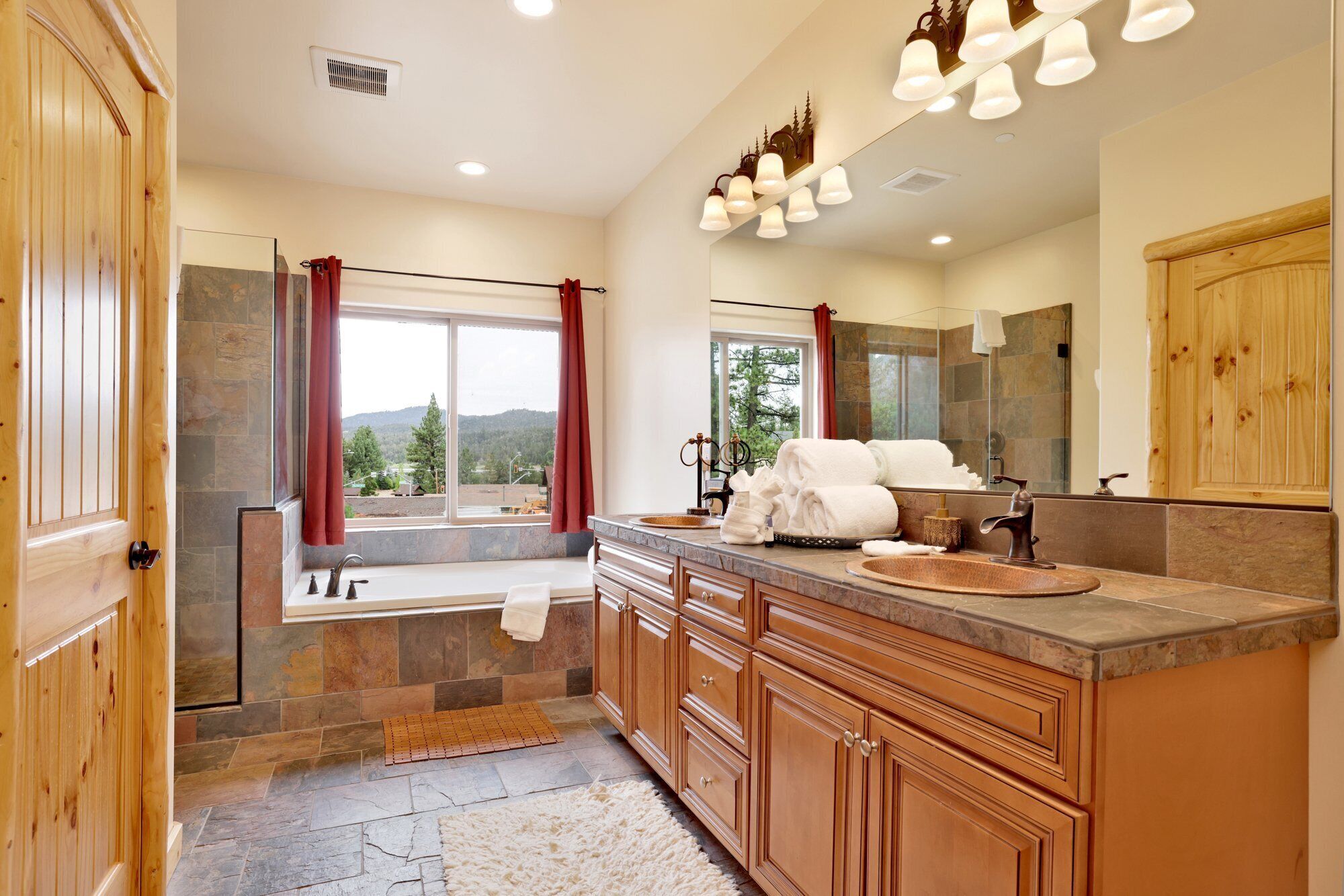 A bathroom with a stone shower, a large mirror, and a view of the outdoors.