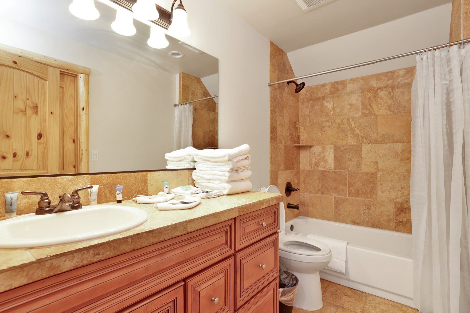 A bathroom with a sink, mirror, vanity, toiletries, a shower, and a toilet.