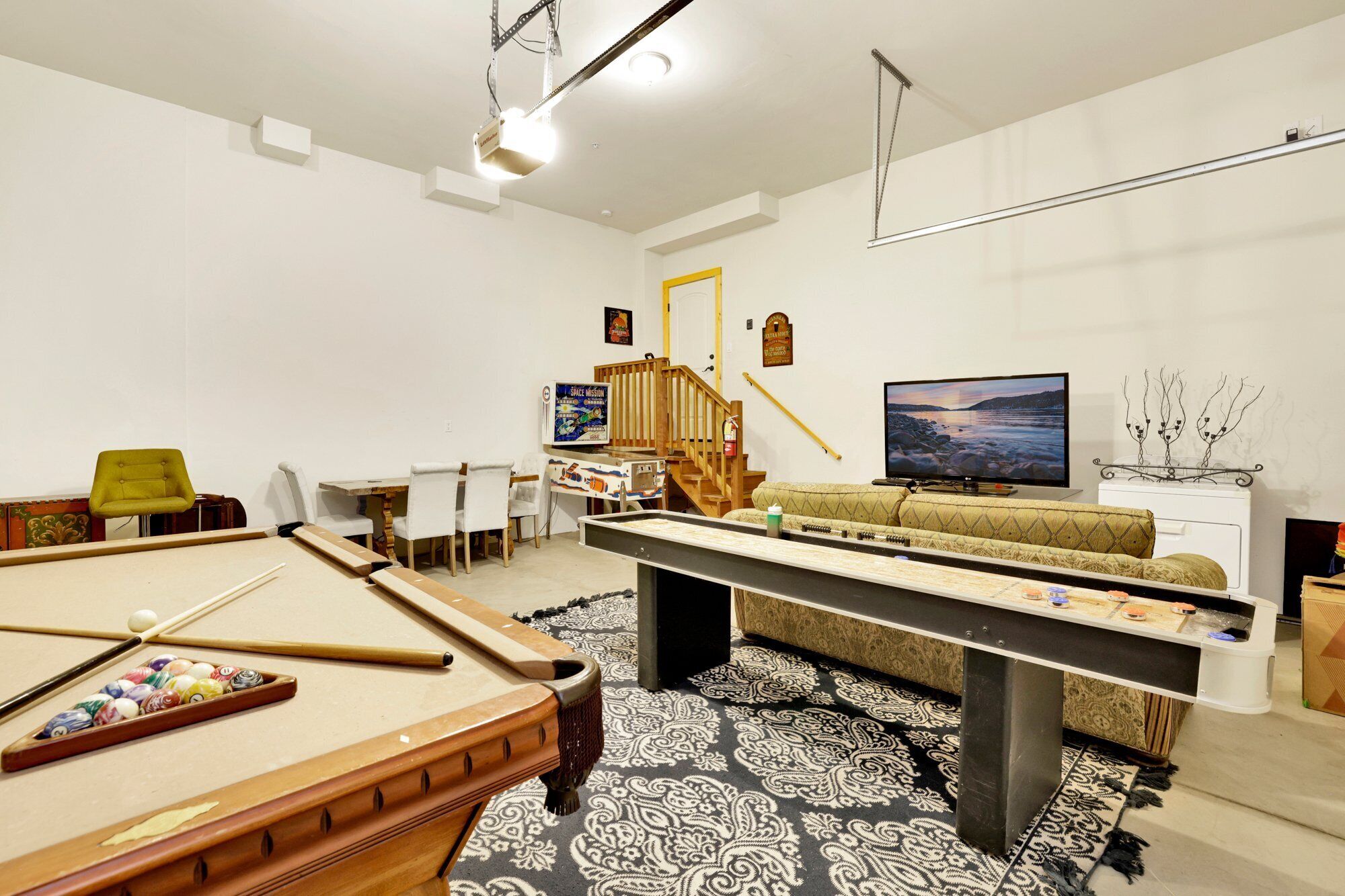 Ein Wohnzimmer mit Billardtisch, einer Couch, einem Fernseher und einer Treppe.