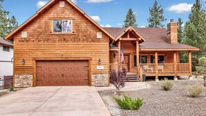 A log cabin with a large garage, a covered porch, and a stone foundation. - Eagle Ridge Views #1648 (Big Bear Lake)