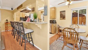 A kitchen with wooden cabinets, a granite countertop, and a dining area with wooden chairs and a table. - Cozy UP TO Summit #1651 (Big Bear Lake)