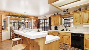 Una cocina con armarios de madera, una isla central, taburetes de bar y vistas al exterior a través de grandes ventanales.