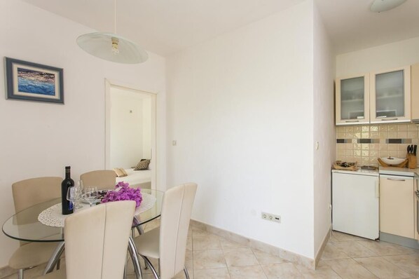 A modern kitchen with white cabinets, a small refrigerator, and a dining area with a glass table and chairs.