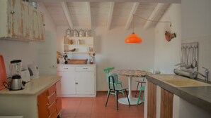 Eine Küche mit gefliestem Boden, weißen Schränken, einer Holzarbeitsplatte, einem Tisch mit Stühlen und einer hängenden, orangefarbenen Pendelleuchte.