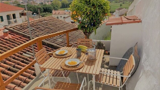 Ein Balkon mit Holztisch, einem Essplatz, einem Metallstuhl und einem Blumentopf mit einem Baum.
