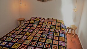 Ein Zimmer mit einer farbenfrohen Häkeldecke, einem Holzhocker und einer an der Wand befestigten Fischskulptur.