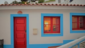 Ein Gebäude mit roter Tür und blauen Fensterrahmen, einem kleinen Briefkasten und einer Treppe, die zum Eingang führt.