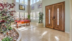 A spacious room with a pool table, large windows, and a wooden door.