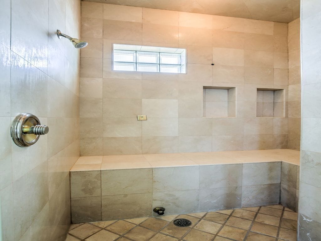 Un espace douche équipé d’un banc, de murs carrelés, d’une fenêtre et d’un drain.