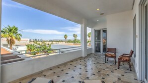 A balcony with a view of palm trees and a cityscape, furnished with chairs and a table.
