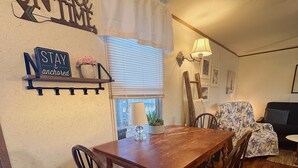 A dining area with a wooden table and chairs, a window with blinds, and decorative wall signs. - Great Hunting, Fishing  and Family Vacation Getaway (Linden)