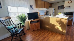 A compact kitchen with wooden cabinets, a built-in stove, and a microwave. There's a dining area with a rocking chair and a small table. - Great Hunting, Fishing  and Family Vacation Getaway (Linden)