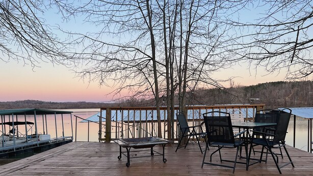 A wooden deck with a table and chairs, overlooking a calm lake. - Great Hunting, Fishing  and Family Vacation Getaway (Linden)