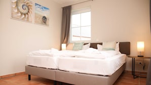 A double bed with white linens, a bedside table with a lamp, and two wall-mounted artworks. - Apartment 3 - Apartment near the beach (Nienhagen)