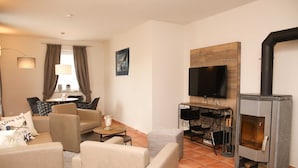 A living room with beige sofas, a TV mounted on the wall, and a wood-burning stove. - Apartment 3 - Apartment near the beach (Nienhagen)