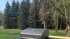 Een draagbare gasgrill met vier branders en een bijzettafel, geplaatst op een houten terras.