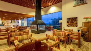 A spacious lobby with a high ceiling, a central fireplace, and a view of the outdoors. - GHL Hotel Lago Titicaca (Puno)