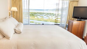 A hotel room with a large bed, a television, and a view of a water body. - GHL Hotel Lago Titicaca (Puno)