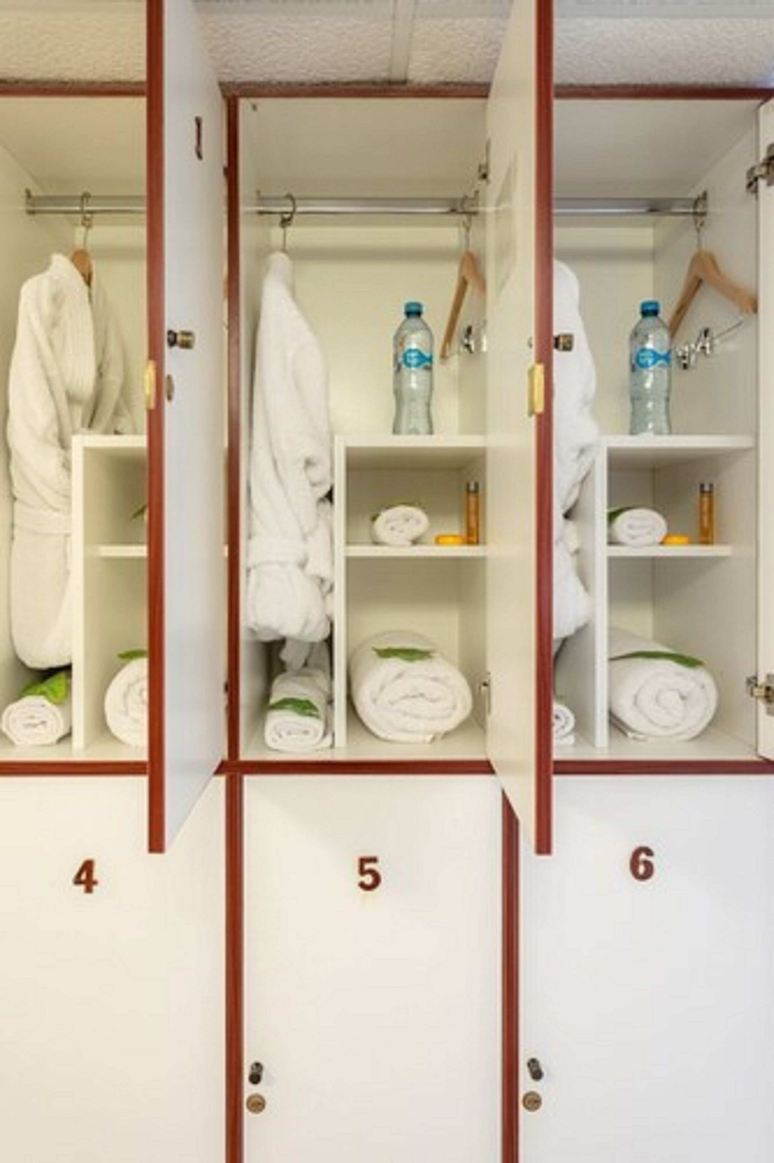 A hotel room with a wardrobe containing numbered compartments, each with folded towels and toiletries.