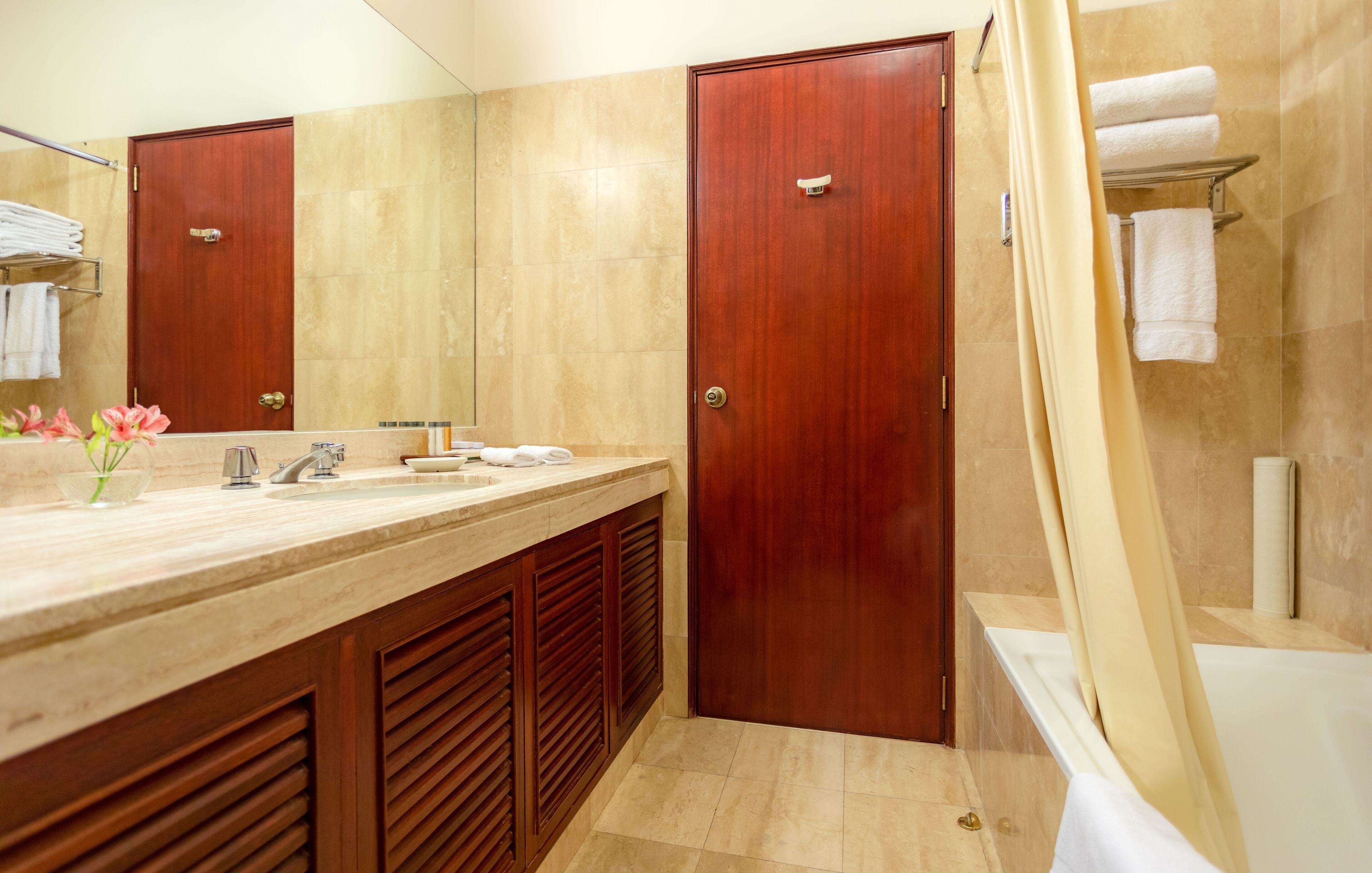 A modern bathroom with a wooden vanity, a large mirror, and a bathtub.