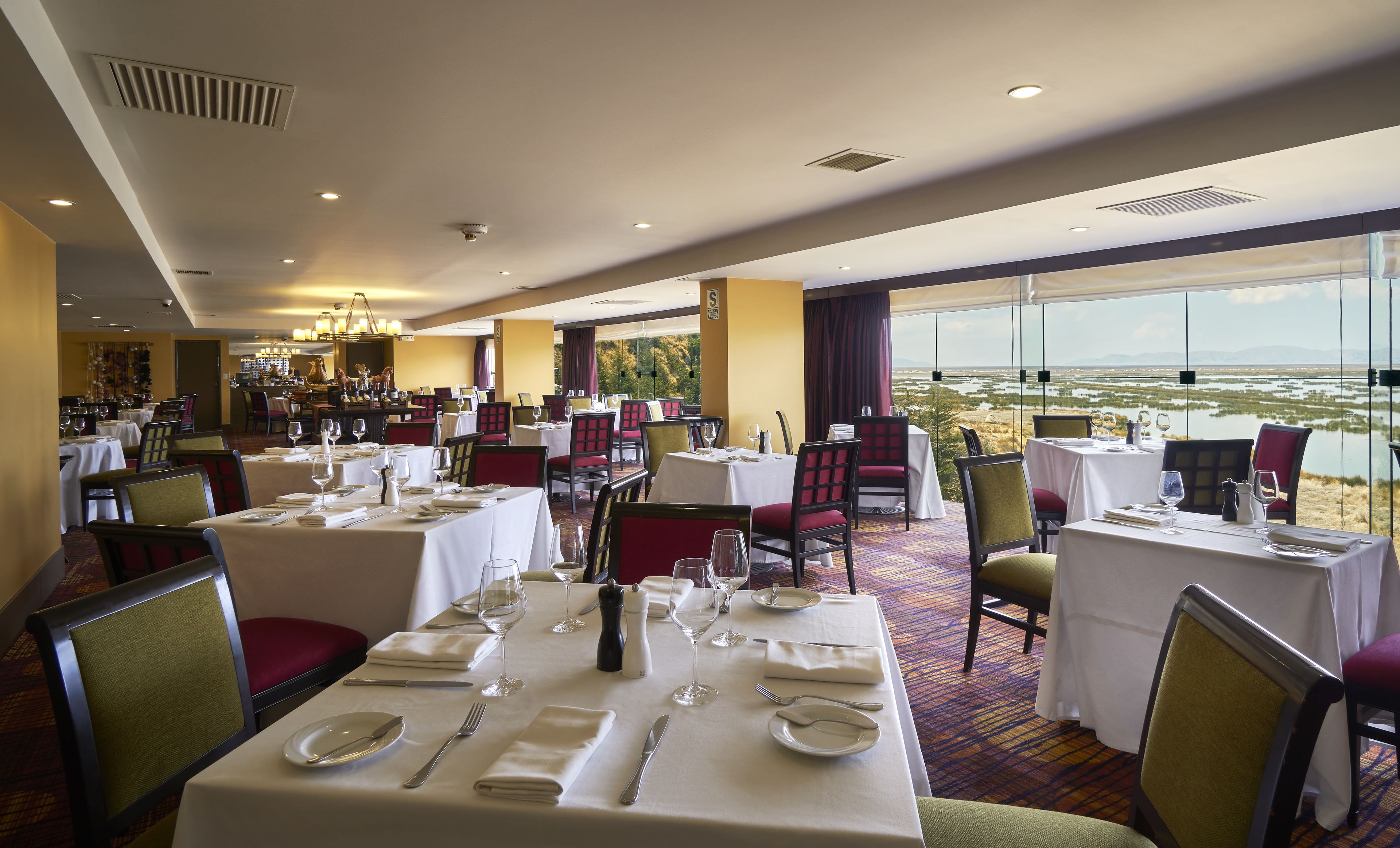 Un restaurante con mesas dispuestas para comer, una zona de bar y vistas a un paisaje a través de amplios ventanales.