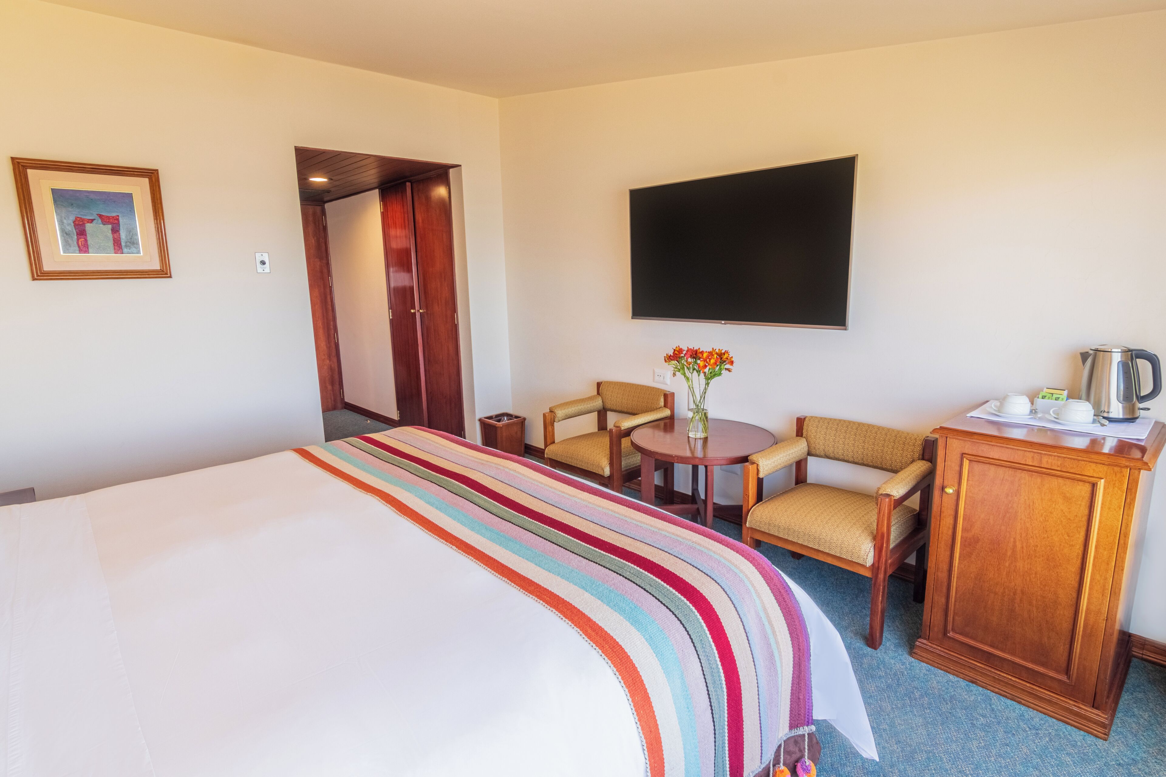 A hotel room with a large bed, a TV, a small table with chairs, and a cabinet.