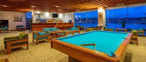 A pool area with a pool table, multiple seating options, and a view of the cityscape.