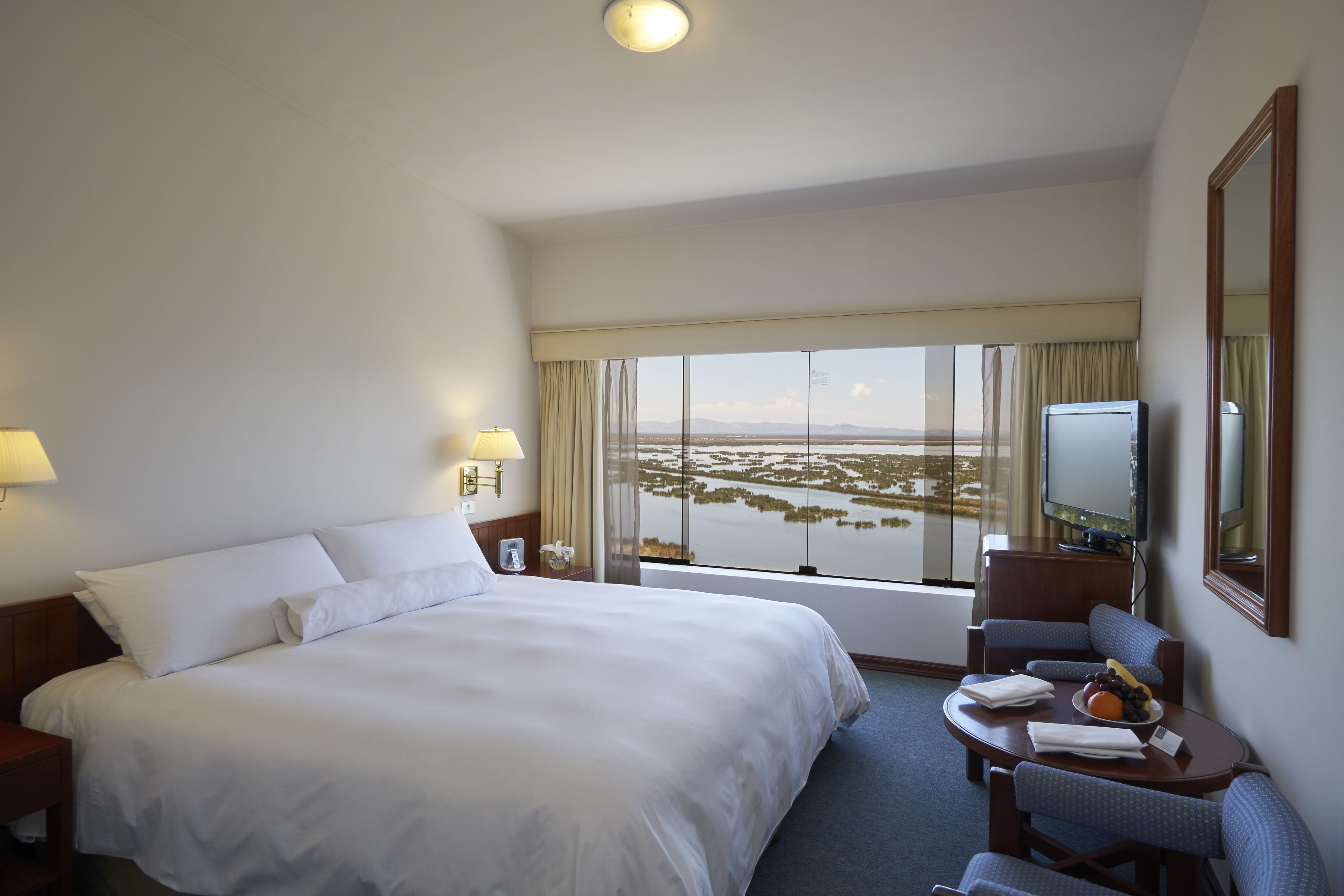 A hotel room with a large bed, a desk with a television, and a view of a body of water.