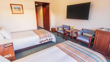 Ein Hotelzimmer mit zwei Betten, einem Fernseher, einem kleinen Tisch mit Stühlen und einer Tür zu einem weiteren Raum.