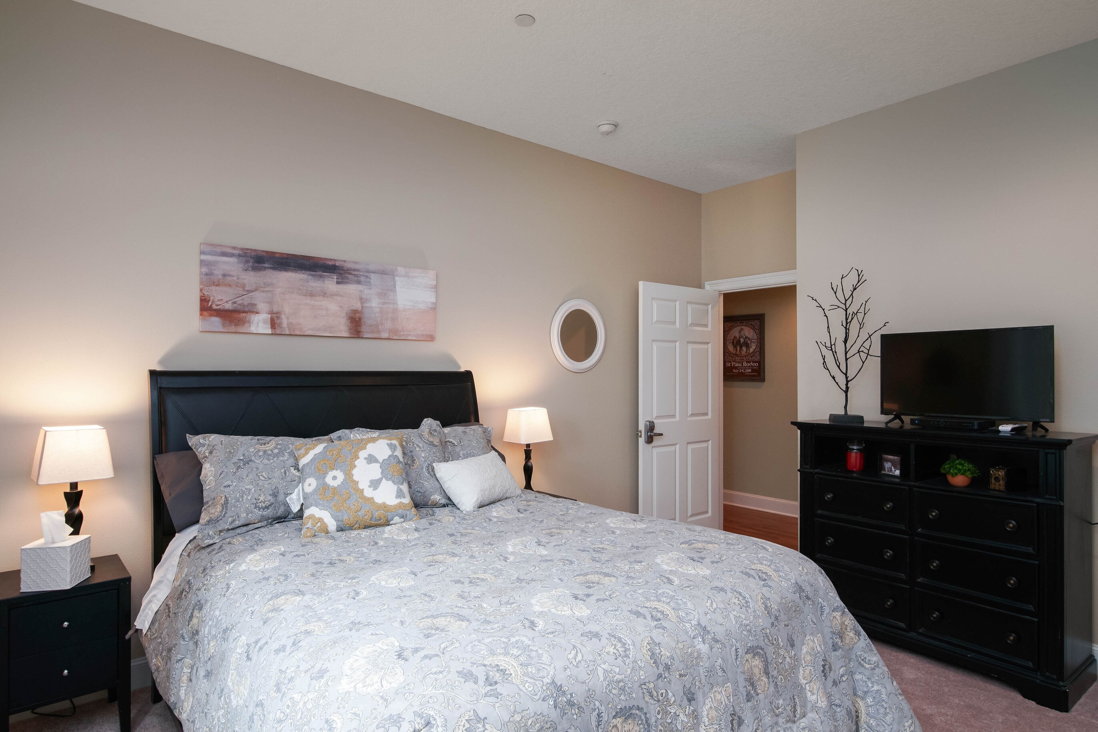 A bedroom with a bed, two bedside tables with lamps, a dresser, a television, and a door.