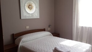 Un letto ben rifatto con copripiumino bianco e un asciugamano piegato di lato.