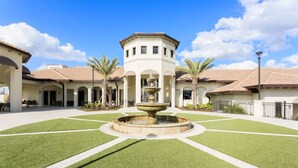 A courtyard with a central fountain, surrounded by palm trees and a building with a tiled roof. - Piece of Heaven Pool Home by AV Dreams (Davenport)