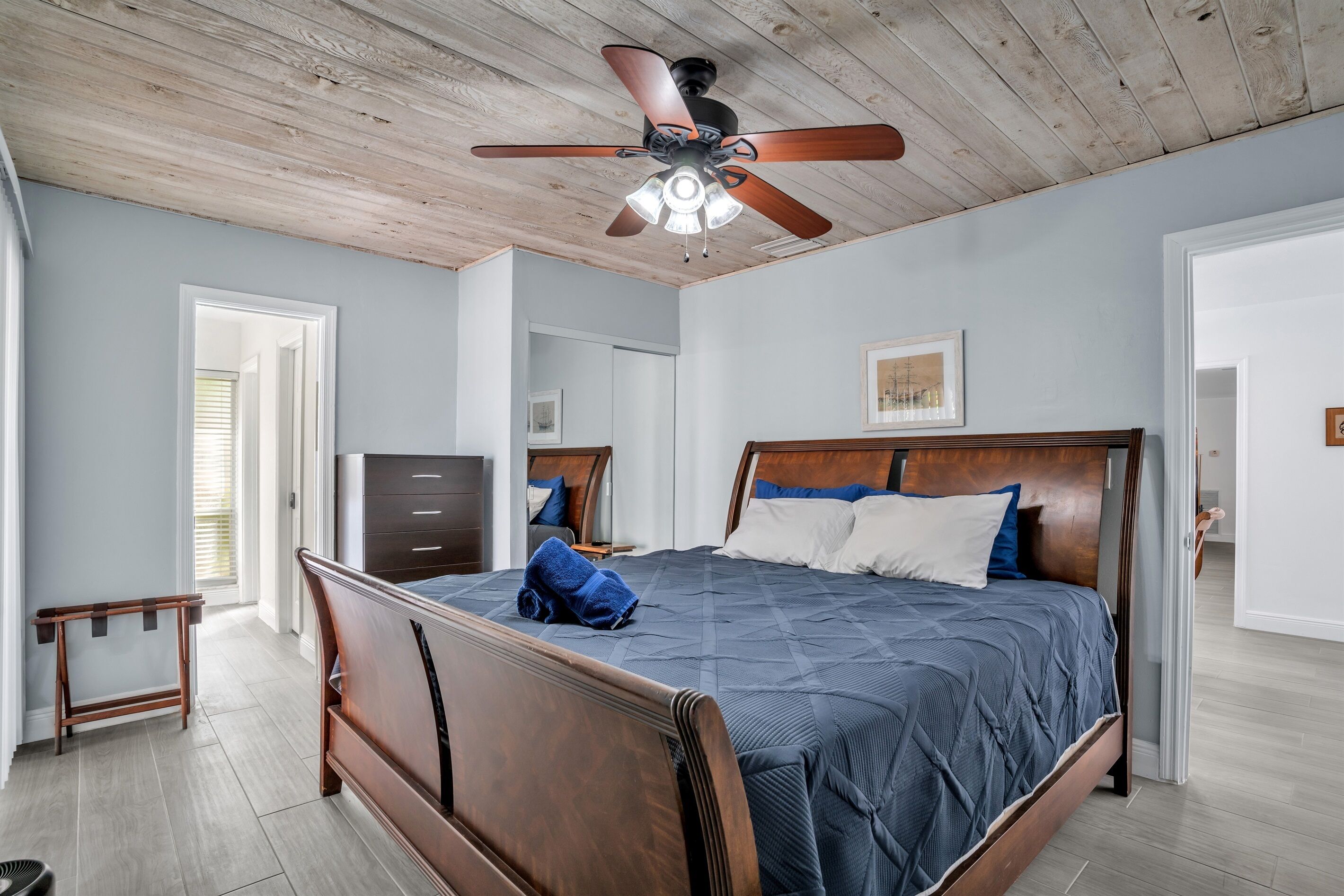 A bedroom with a wooden bed, a ceiling fan, and a view of the outside.