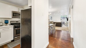 Eine moderne Küche mit Edelstahlgeräten, ein Essbereich mit Holzboden und Blick in ein Wohnzimmer.