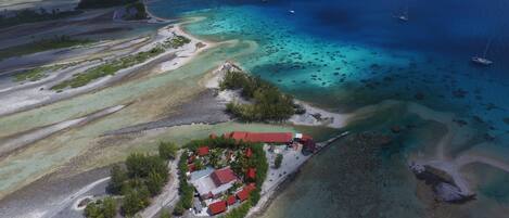An aerial view of a coastal property with a red-roofed building, clear blue waters, and boats.