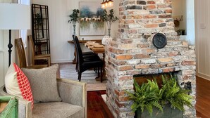 A living room with a stone fireplace, a dining area with wooden furniture, and a cozy seating area with a chair and ottoman. - The RED DOOR: Explore Pensacola's Downtown Entertainment next to Wedding Venues! (Pensacola)