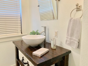 Une salle de bain avec un lavabo sur colonne blanc, une petite plante en pot, un flacon de savon liquide et une serviette suspendue à un porte-serviettes en métal.